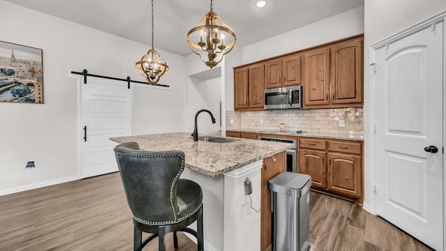 kitchen featuring backsplash, a barn door, appliances with stainless steel finishes, a sink, and wood finished floors