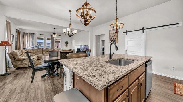 kitchen with a barn door, ceiling fan with notable chandelier, wood finished floors, a sink, and dishwasher