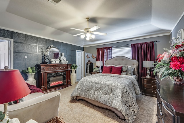 bedroom with carpet, a tray ceiling, a fireplace, visible vents, and a ceiling fan