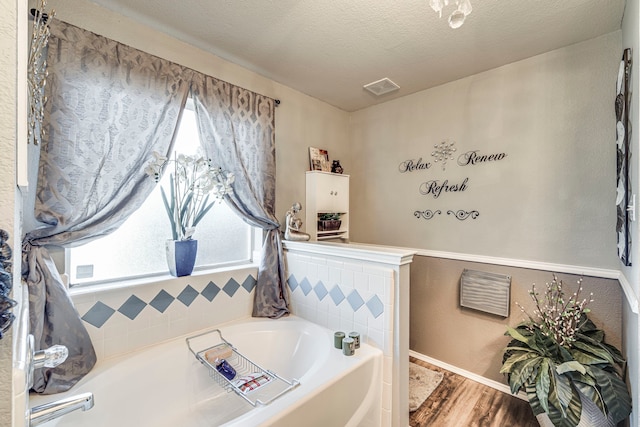 full bath featuring visible vents, a garden tub, a textured ceiling, and wood finished floors