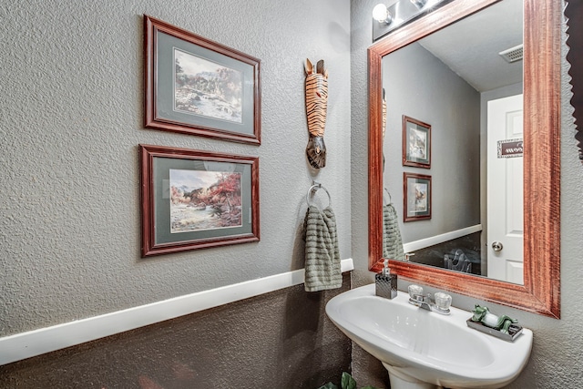 bathroom featuring baseboards, visible vents, a sink, and a textured wall