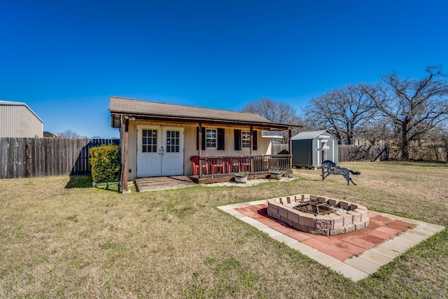 back of house with an outdoor fire pit, a fenced backyard, a storage shed, an outdoor structure, and a lawn