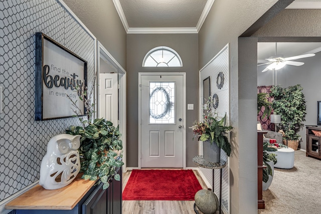 foyer featuring ceiling fan, a textured ceiling, wood finished floors, baseboards, and crown molding