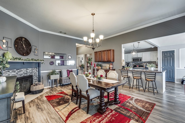 dining space with a tile fireplace, a notable chandelier, crown molding, and light wood finished floors