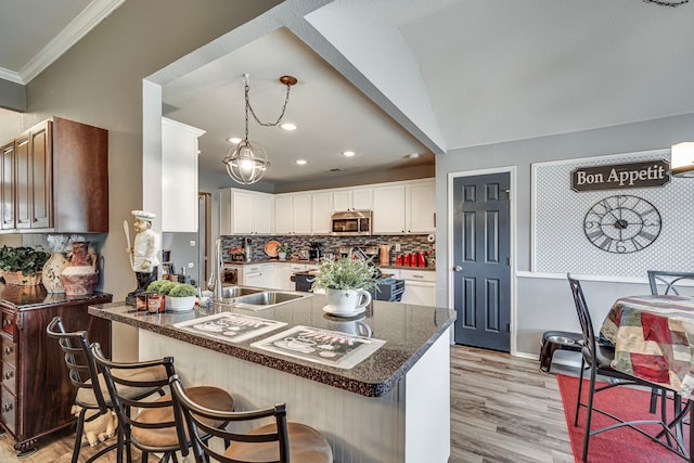 kitchen featuring tasteful backsplash, light wood-style flooring, stainless steel microwave, a peninsula, and white cabinetry