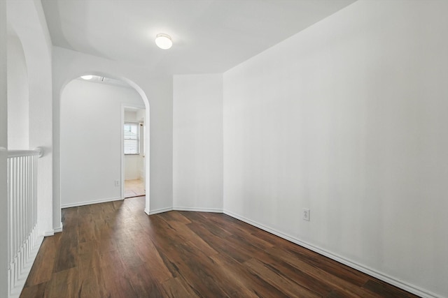 empty room with arched walkways, wood finished floors, and baseboards