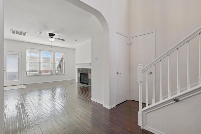 unfurnished living room with stairs, visible vents, a tiled fireplace, and wood finished floors