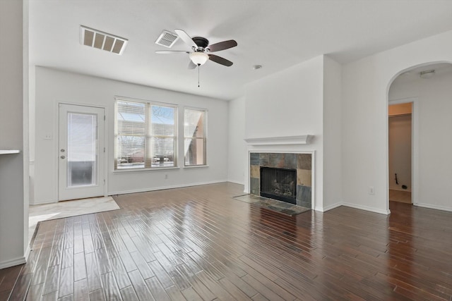 unfurnished living room with arched walkways, a fireplace, visible vents, ceiling fan, and wood finished floors