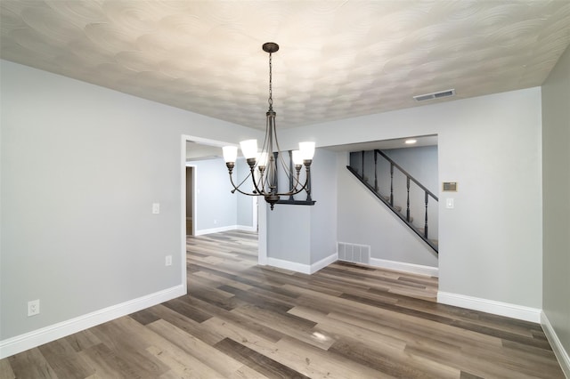 unfurnished dining area featuring baseboards, stairs, visible vents, and wood finished floors