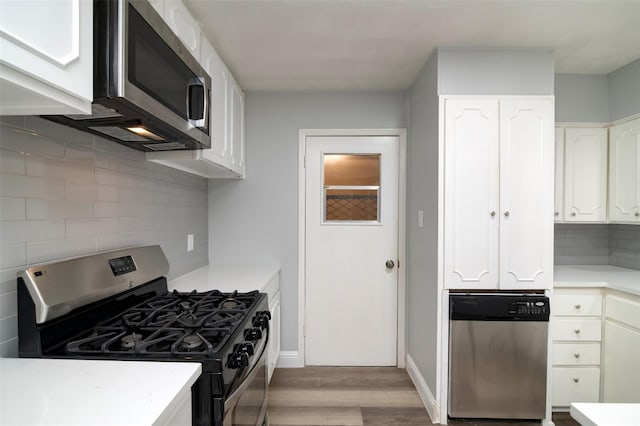 kitchen with light wood-style floors, white cabinets, light countertops, appliances with stainless steel finishes, and tasteful backsplash