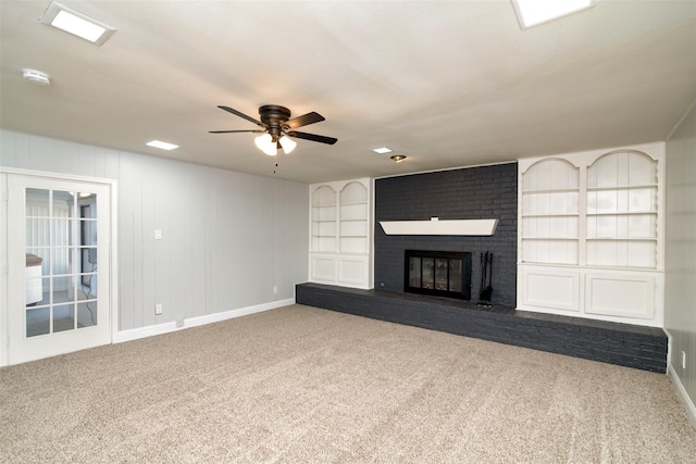 unfurnished living room featuring built in features, carpet, a ceiling fan, a brick fireplace, and baseboards