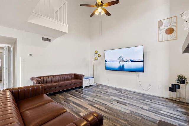 living area with baseboards, visible vents, a ceiling fan, a towering ceiling, and wood finished floors