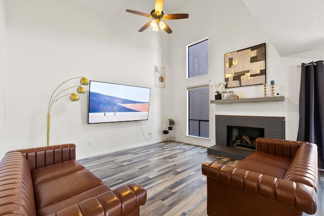 living area featuring baseboards, ceiling fan, wood finished floors, a fireplace, and high vaulted ceiling