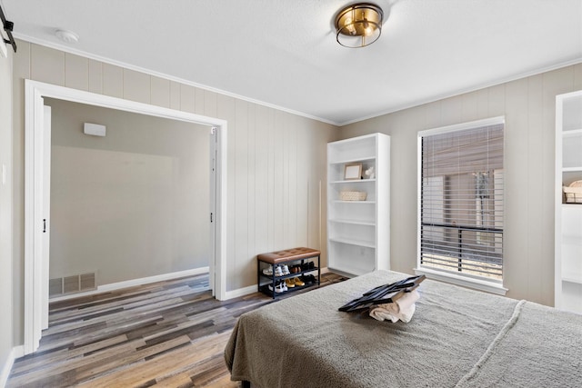 bedroom featuring ornamental molding, wood finished floors, visible vents, and baseboards