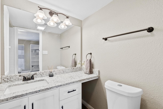 bathroom with a textured wall, vanity, and toilet