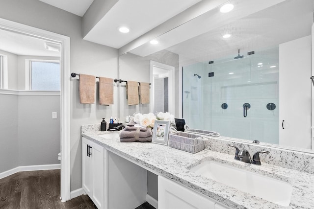 full bath with wood finished floors, a sink, baseboards, a shower stall, and double vanity