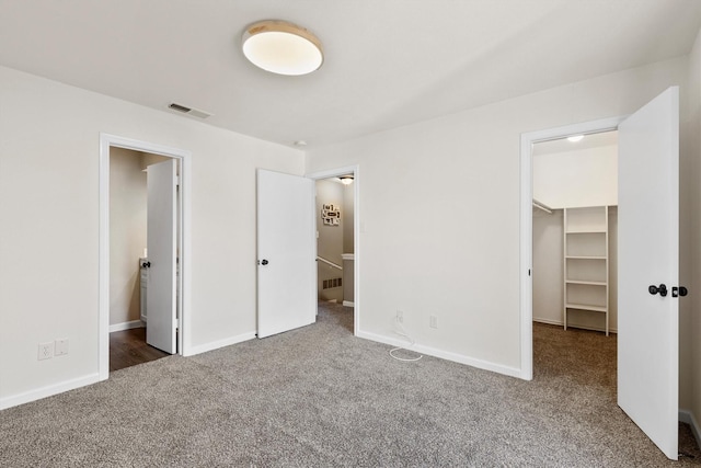 unfurnished bedroom featuring baseboards, visible vents, a walk in closet, and carpet flooring