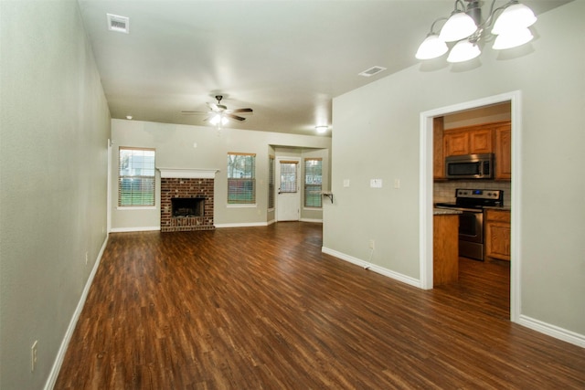 unfurnished living room with a fireplace, visible vents, dark wood-type flooring, and ceiling fan with notable chandelier