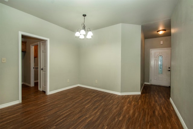 spare room featuring a chandelier, dark wood-style flooring, and baseboards