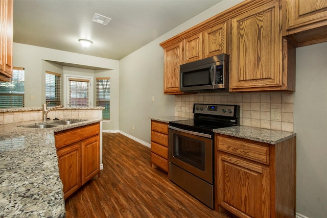 kitchen featuring visible vents, brown cabinetry, dark wood-style flooring, stainless steel appliances, and a sink