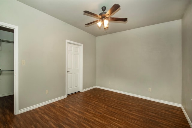 unfurnished bedroom featuring a walk in closet, a closet, ceiling fan, wood finished floors, and baseboards