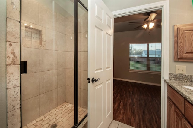 full bathroom featuring ceiling fan, wood finished floors, vanity, baseboards, and a shower stall