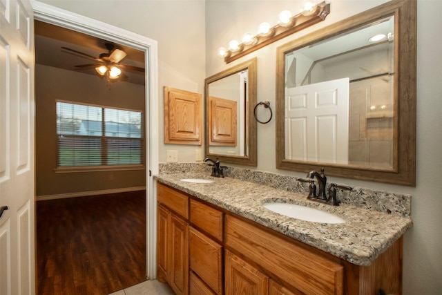 bathroom featuring a ceiling fan, double vanity, a sink, and wood finished floors