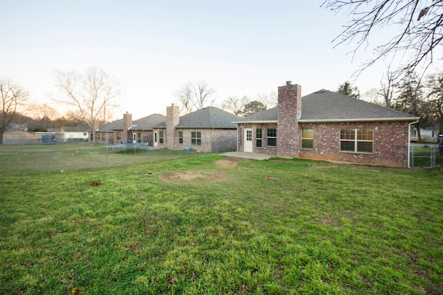 rear view of property featuring a trampoline, brick siding, a yard, a chimney, and fence