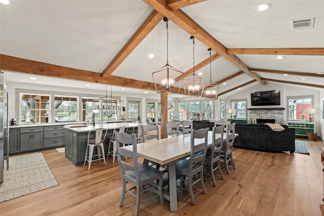 dining room with visible vents, lofted ceiling with beams, a healthy amount of sunlight, light wood-style floors, and a fireplace