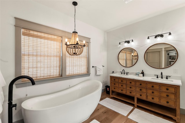 full bathroom with a freestanding tub, double vanity, a sink, and wood finished floors