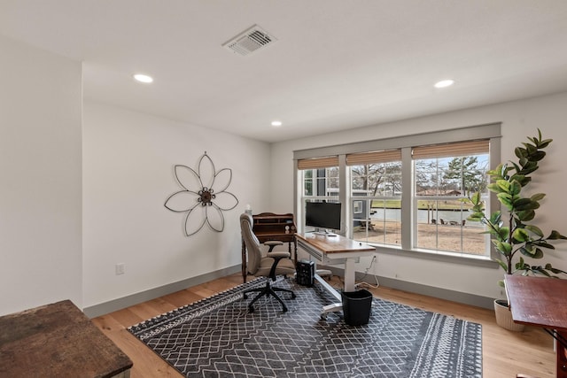 office area with light wood-type flooring, visible vents, and baseboards