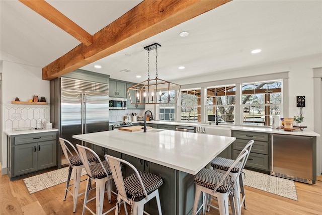 kitchen featuring beam ceiling, stainless steel appliances, tasteful backsplash, light countertops, and light wood-style floors