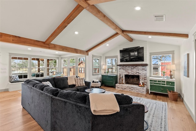 living room featuring vaulted ceiling with beams, visible vents, baseboards, light wood-type flooring, and a brick fireplace