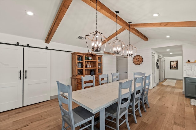 dining room featuring light wood-type flooring, visible vents, lofted ceiling with beams, and a barn door