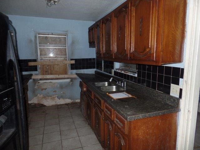 kitchen featuring light tile patterned floors, black fridge, brown cabinetry, and a sink