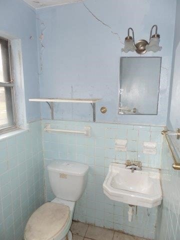 bathroom featuring wainscoting, toilet, a sink, tile patterned flooring, and tile walls