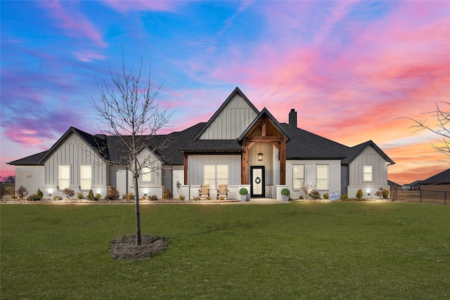 view of front of house with a shingled roof, a chimney, board and batten siding, and a yard