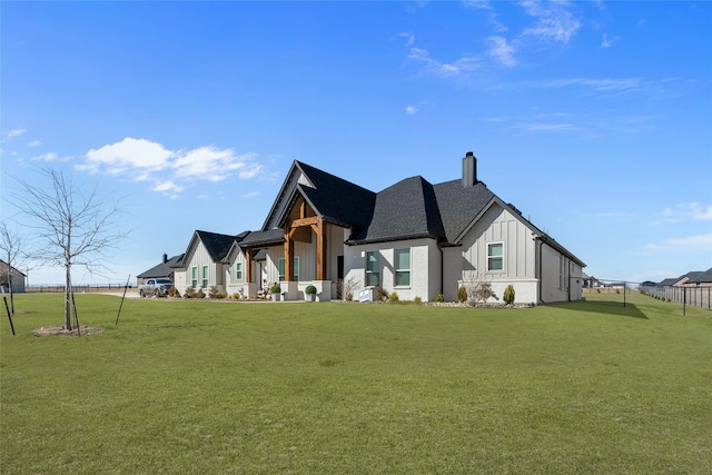 view of front of home with board and batten siding, a front yard, a shingled roof, and a chimney