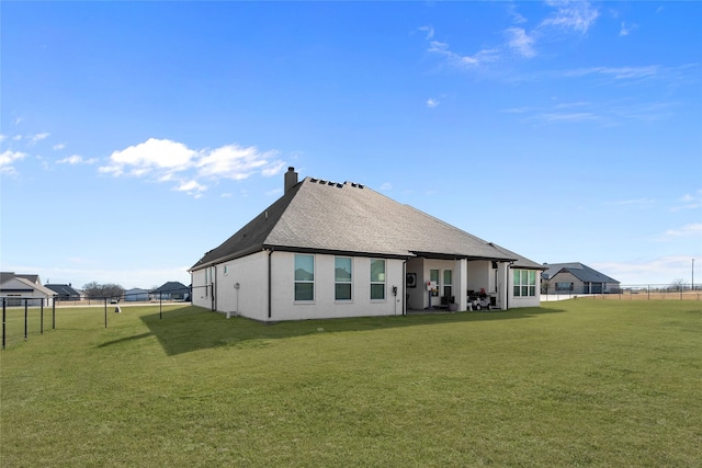 rear view of property with roof with shingles, a chimney, fence, and a yard