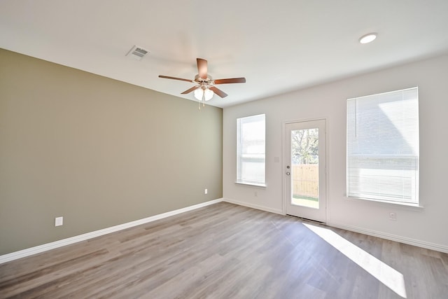 empty room with a ceiling fan, wood finished floors, visible vents, and baseboards