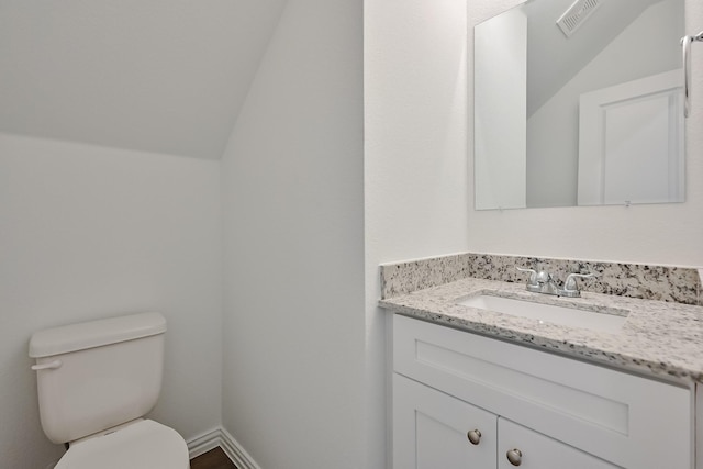 bathroom with toilet, vanity, visible vents, vaulted ceiling, and baseboards