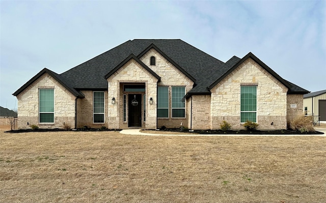 french provincial home with brick siding, roof with shingles, and a front yard