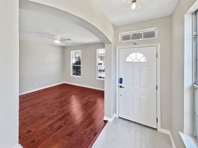 foyer entrance featuring baseboards, arched walkways, ceiling fan, and wood finished floors