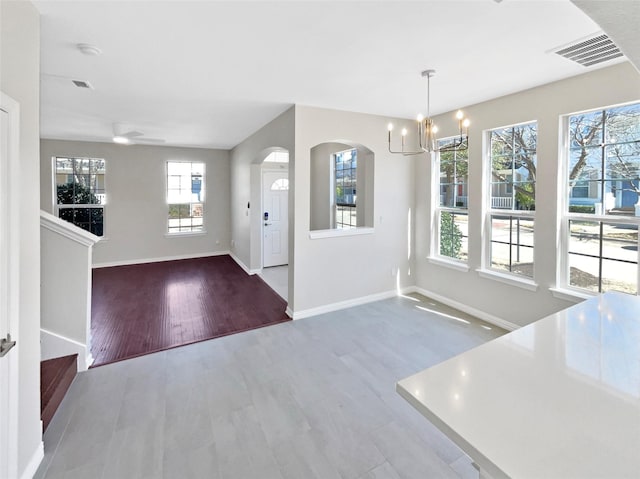 entryway with arched walkways, visible vents, wood finished floors, a chandelier, and baseboards