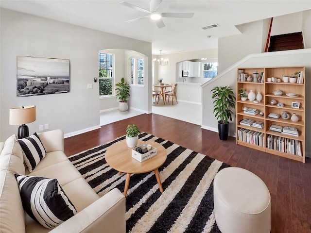 living room featuring ceiling fan with notable chandelier, wood finished floors, visible vents, and baseboards