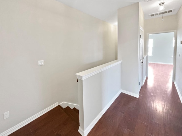 hallway with attic access, visible vents, baseboards, and wood finished floors