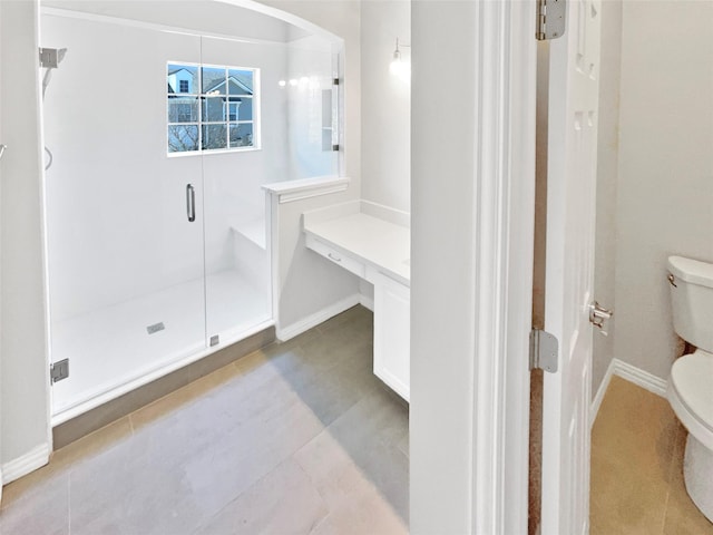 bathroom with a stall shower, toilet, and baseboards