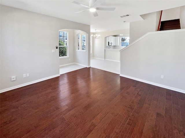 unfurnished living room featuring dark wood-style floors, baseboards, visible vents, and ceiling fan with notable chandelier