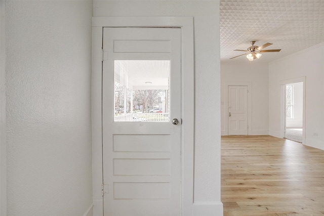 doorway featuring light wood-style flooring, baseboards, ceiling fan, and a textured wall