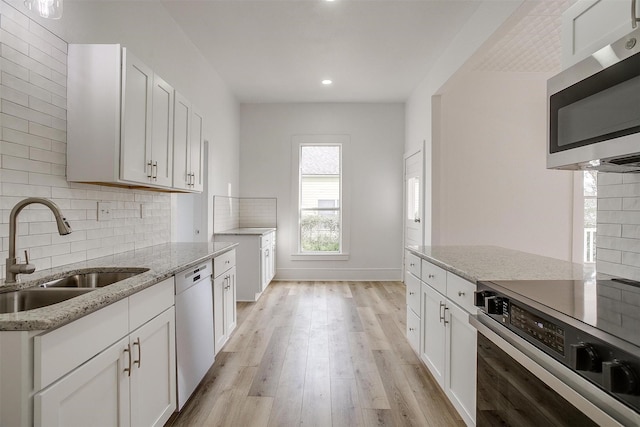 kitchen featuring range, dishwasher, stainless steel microwave, light stone countertops, and a sink